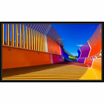 A Sharp 50″ 4K UHD Professional Display showing a vibrant, multicolored pedestrian bridge with curved walls and slatted railings against a blue sky.